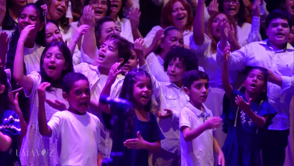 Crianças do Coral Uma Voz cantando de braços erguidos no palco